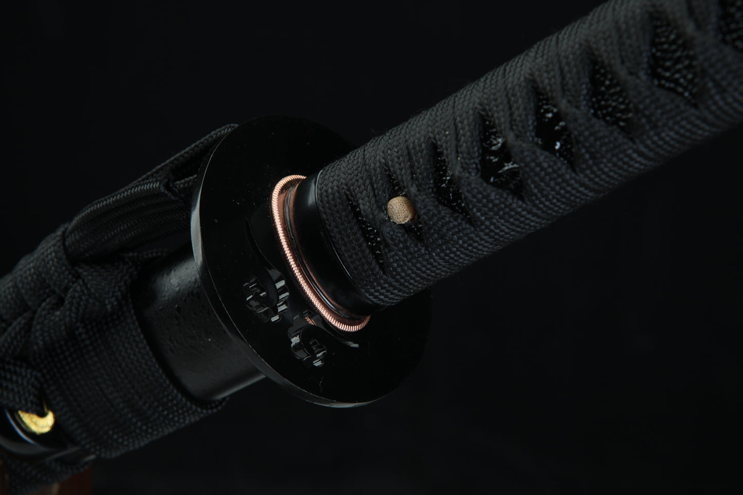 Close-up of a black sword handle with gold accents on a dark background