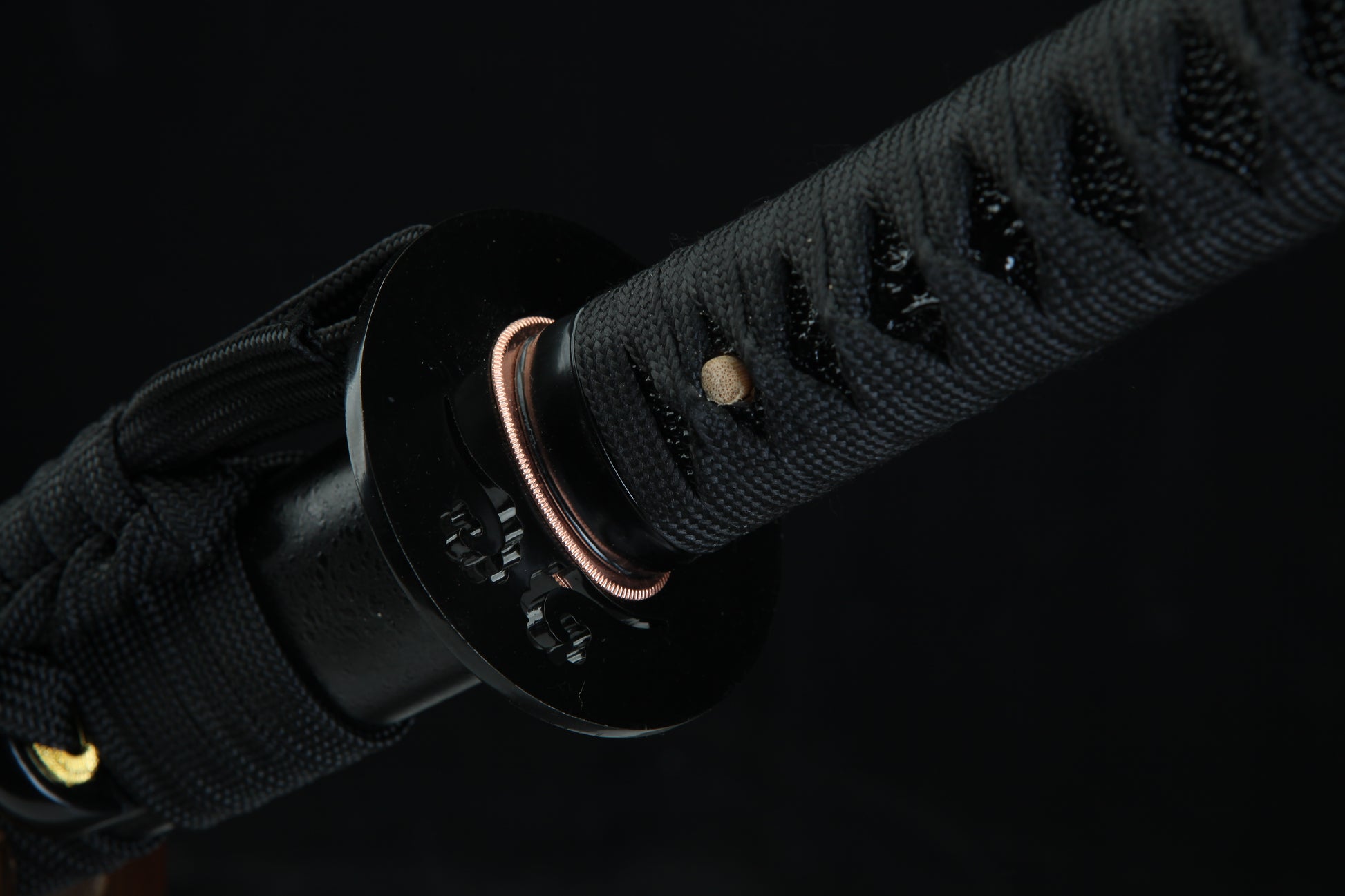 Close-up of a black sword handle with gold accents on a dark background