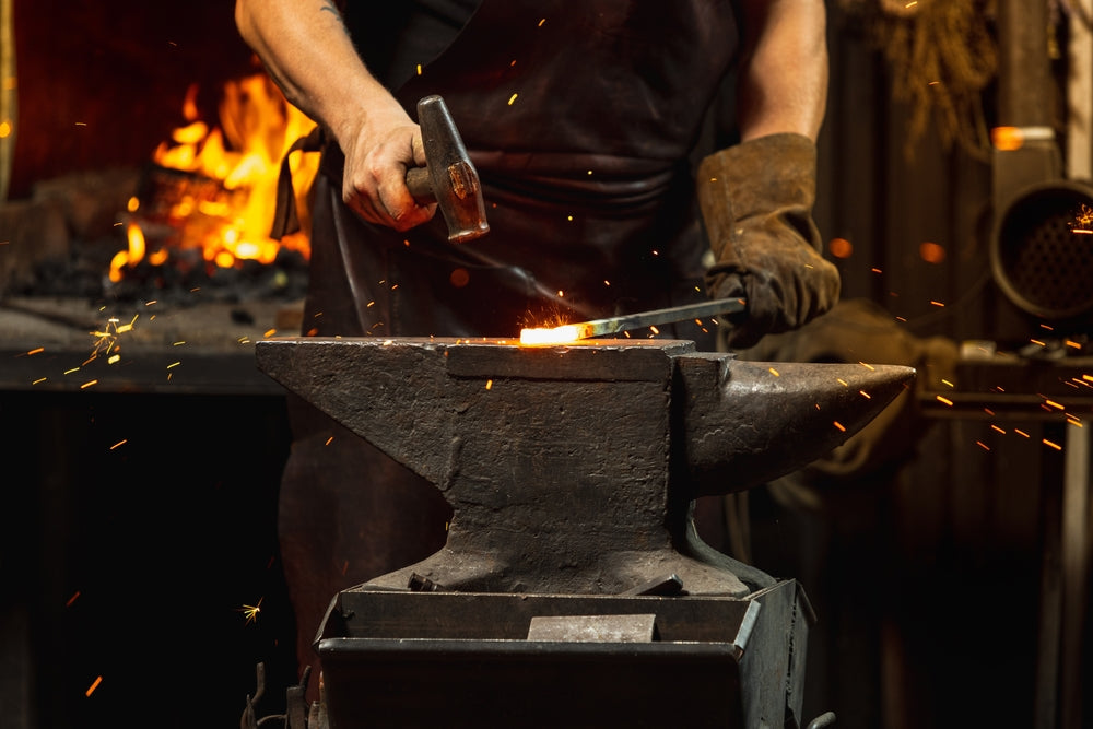Person working with hot metal on an anvil in a forge setting