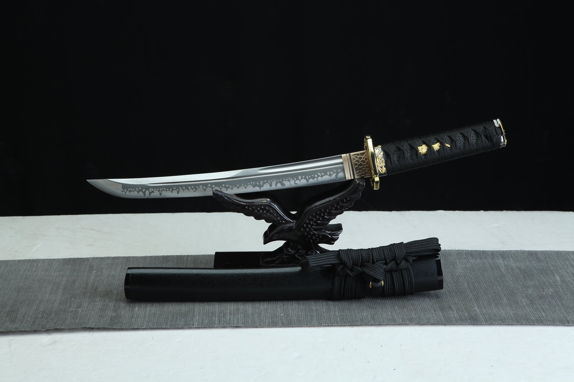 TANTO Sword Damascus Steel Blade with a black sheath on a gray surface against a black background