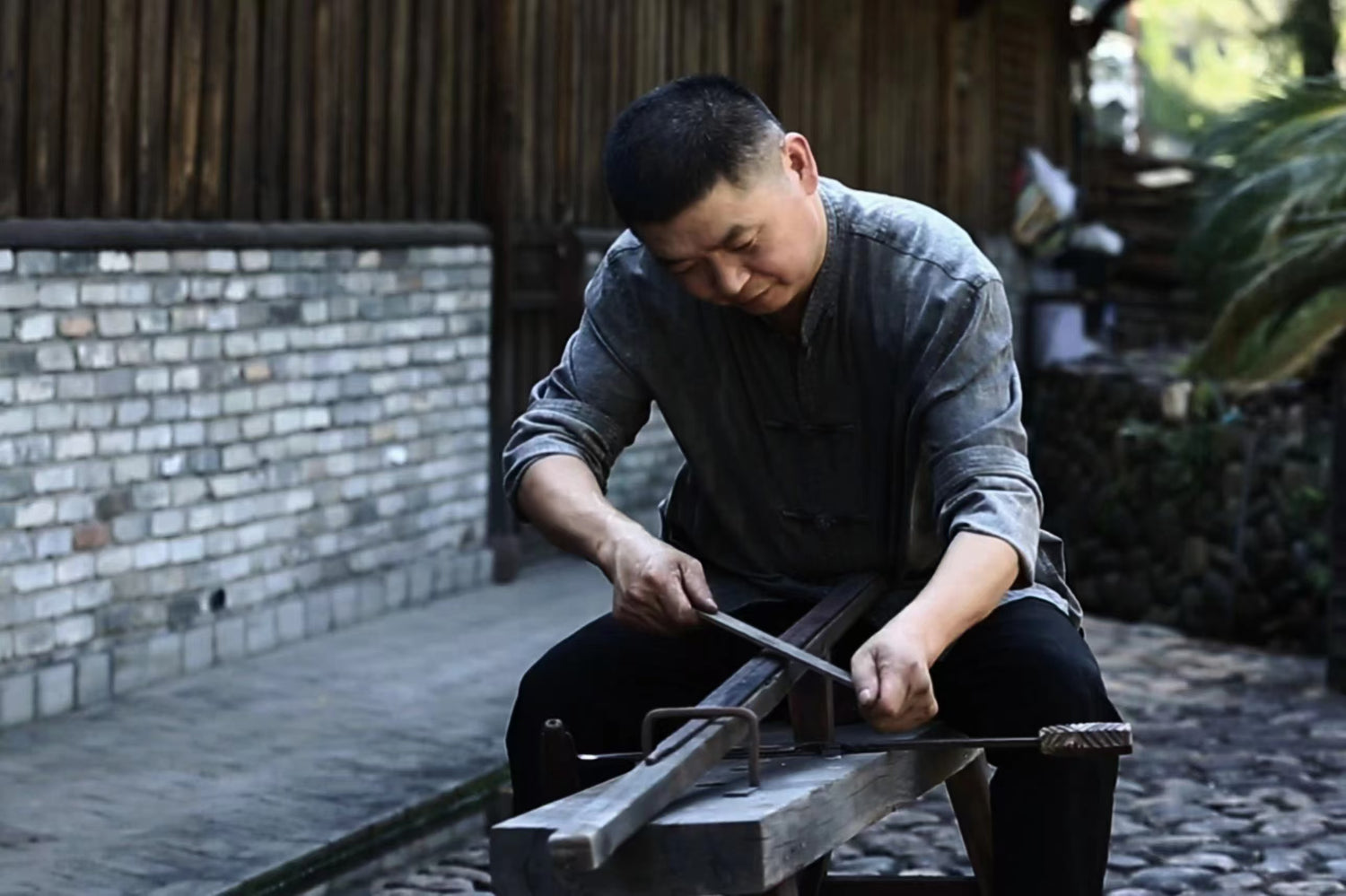 Zhao Peiyan, a master bladesmith from Zhejiang Province, Chinawith metal tools outdoors near a brick wall
