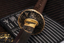 A photo of Moonswords Banrin Katana with a bronze guard, is shown against a dark, slatted bamboo mat background.