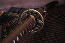 A photo of Moonswords Banrin Katana with a bronze guard, is shown against a dark, slatted bamboo mat background.