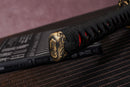 Close-up of Moonswords Chi no bara katana handle with intricate designs on a textured surface.