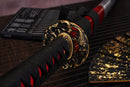 A photo of Moonswords Chi no bara Katana with a bronze guard, is shown against a dark, slatted bamboo mat background.