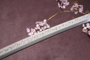 A close-up view of a Clay-Tempered T10 Steel blade against a textured background.