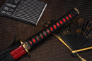 A close-up view of Moonswords Chi no bara Katana with bronze guard, black handle and red shealth.