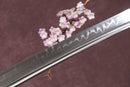 A close-up view of a Clay-Tempered T10 Steel blade against a textured background.
