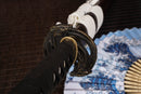 A photo of Moonswords Ghost of Yotei Katana with a bronze guard, is shown against a dark, slatted bamboo mat background.