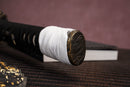 A single katana with a black handle and white accents on the stand is shown against a textured background.