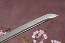 A close-up view of a clay-tempered Damascus steel blade against a textured background