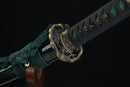 Close-up of a sword with green cord and gold decorative elements on a black background