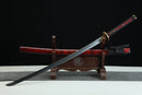 Sword with red blade and black handle on a wooden stand against a dark background