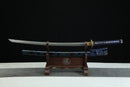 A blue and gold Japanese-style sword is displayed on a wooden stand against a black background.