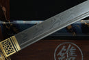 A close-up view of a decorative sword blade with intricate patterns and designs, resting on a wooden surface.