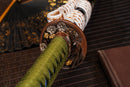 A photo of Moonswords Kyochiku Katana with a silver and gold gilded bronze guard, is shown against a dark, slatted bamboo mat background.