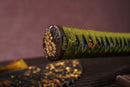 A photo of Moonswords Kyochiku Katana with a silver and gold gilded bronze guard, is shown against a dark, slatted bamboo mat background.