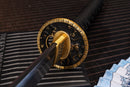A photo of Moonswords Kyoyu Katana in black, with a bronze guard, is shown against a dark, slatted bamboo mat background