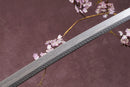 A close-up view of a Clay-Tempered Damascus Steel blade against a textured background.