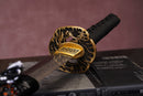 A photo of Moonswords Seima Guren Katana in black, with a bronze guard, is shown against a dark, slatted bamboo mat background.