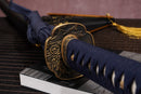 A photo of Moonswords Shuen no Bara  Katana in deep blue, with a bronze guard, is shown against a dark, slatted bamboo mat background.