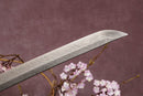 A close-up view of a sharp, pointed Damascus blade with textures against a textured background.