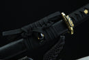 A close-up view of a black and gold sword with a black handle and a black blade, tied with a black string.