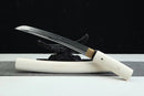 A white-handled Byakuga (白牙) Clay-Tempered T10 Steel Shirasaya Tanto with a black blade rests on a black-and-white striped surface.
