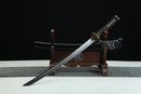 A Japanese-style sword with a black handle and gold accents is displayed on a wooden stand against a black background.