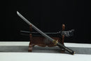 A Japanese-style sword with a black handle and gold accents is displayed on a wooden stand against a black background.