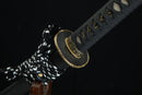 A close-up view of a black and white Japanese-style sword with a decorative metal piece on the blade.