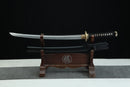 A Japanese-style sword with a black handle and gold accents is displayed on a wooden stand against a black background.